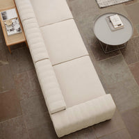 Beige modular sofa with textured vertical patterns, complemented by a round gray side table on a stone tile floor.