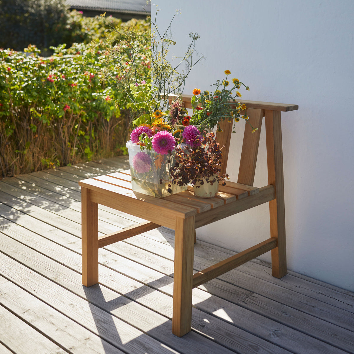 Wooden chair with natural finish, adorned with vibrant flowers in pastel and bright colors, set against a sunny backdrop.