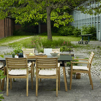 Wooden outdoor dining set featuring beige cushions and a sleek black table surrounded by green foliage.