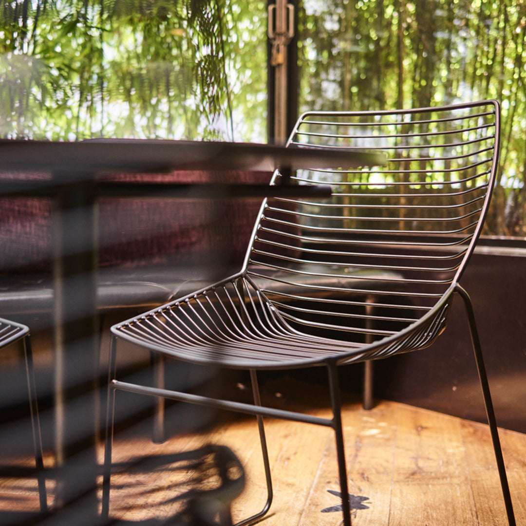Modern black wire chair with sleek, horizontal lines and a minimalist design, set against a natural backdrop.