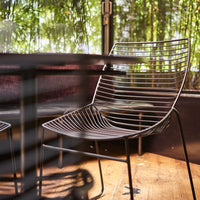 Modern black wire chair with sleek, horizontal lines and a minimalist design, set against a natural backdrop.