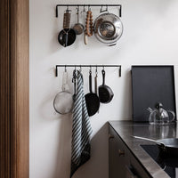 Black metal hanging rack with silver pots and a striped gray and white towel in a modern kitchen setting.