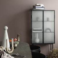 Modern black cabinet with frosted glass doors, against a soft pink wall, featuring minimalist design elements.
