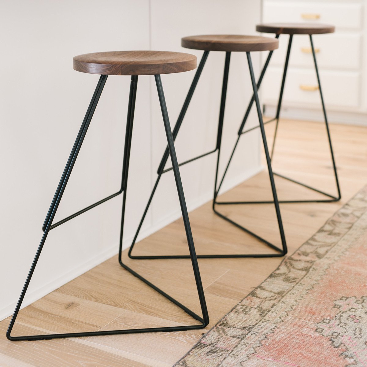 Set of three modern bar stools with wooden seats and sleek black metal legs, featuring a minimalist design.