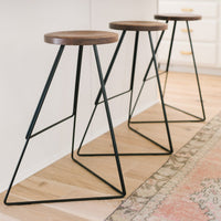 Set of three modern bar stools with wooden seats and sleek black metal legs, featuring a minimalist design.