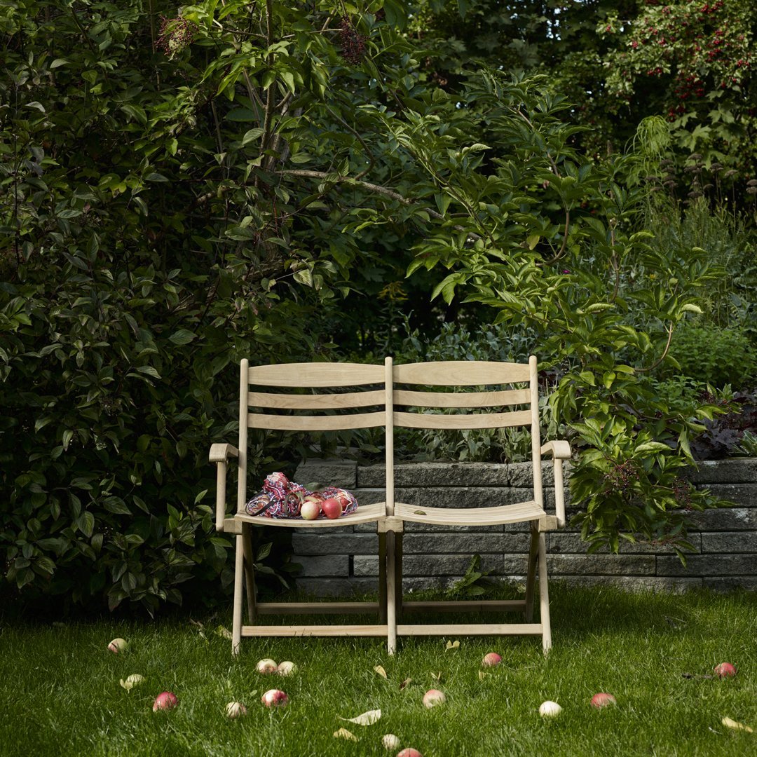 "Light wood outdoor bench surrounded by lush green plants and scattered apples on a vibrant grassy lawn."