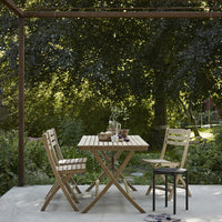 "Natural wood finish patio furniture set with a striped table and matching chairs against a lush green backdrop."