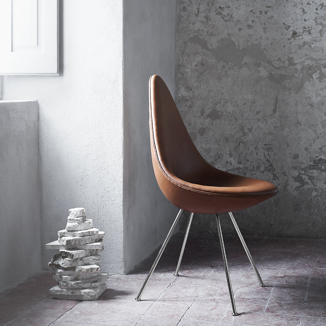 Elegant brown curved chair with sleek silver legs, set against a gray textured wall and rustic flooring.