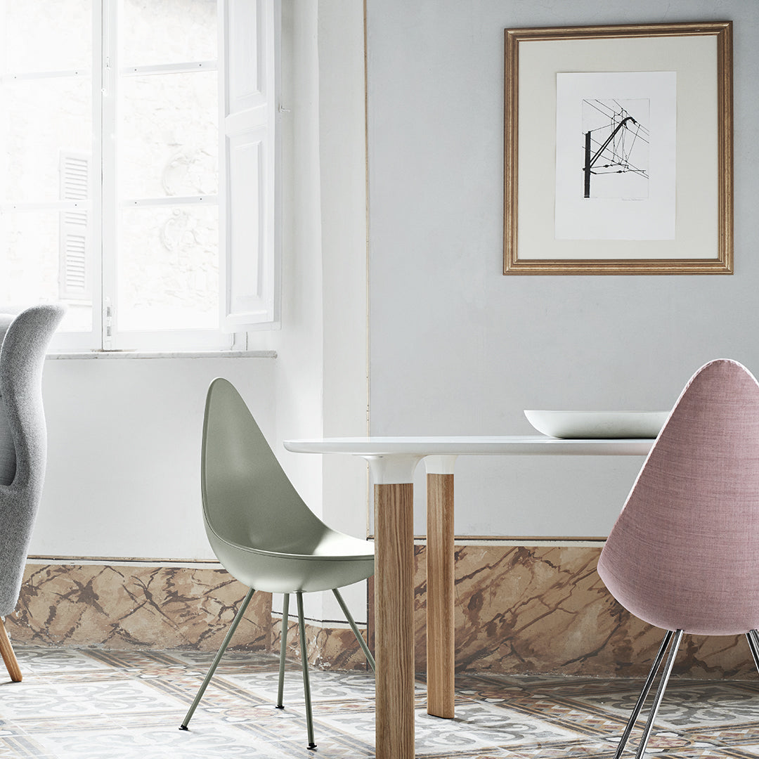 Modern dining area featuring gray, mint green, and blush pink chairs with a light wood table against a patterned floor.