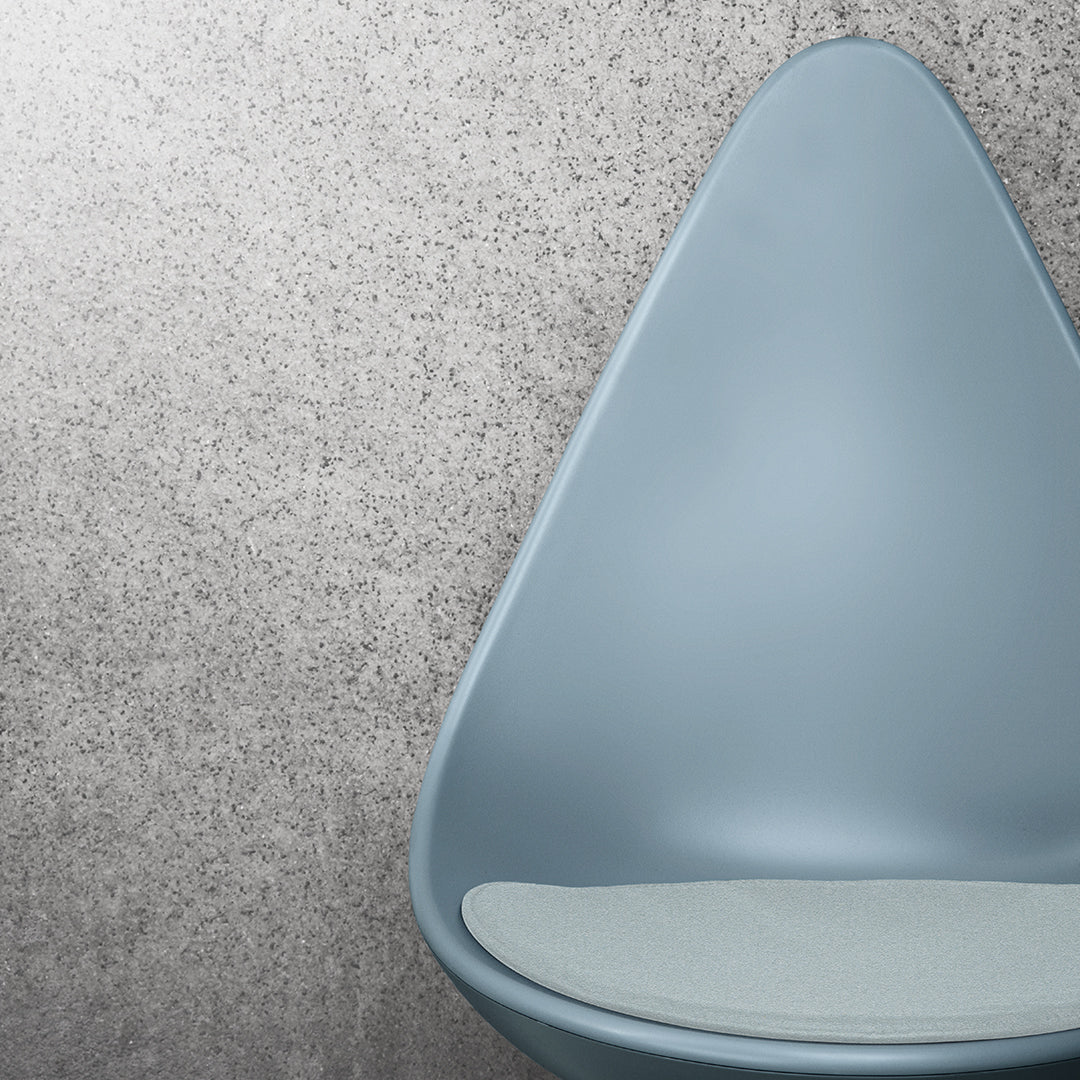 "Stylish blue chair with a smooth, teardrop shape and light gray cushion, set against a textured gray background."