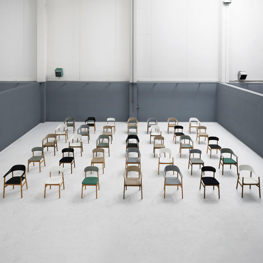 Array of minimalist chairs featuring black, white, gray, and natural wood tones in a spacious, modern setting.