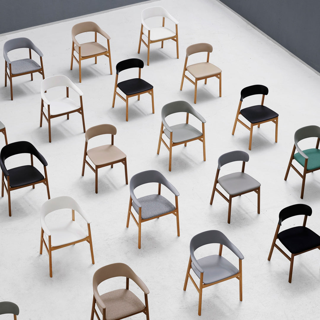 Colorful chairs in various shades of black, gray, beige, and green arranged on a minimalist white floor.