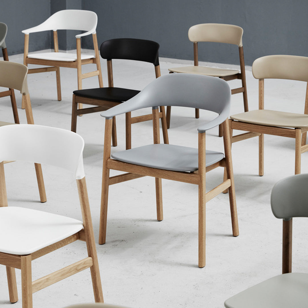 Various modern chairs in white, black, gray, and beige with smooth, minimalistic designs and wooden legs.