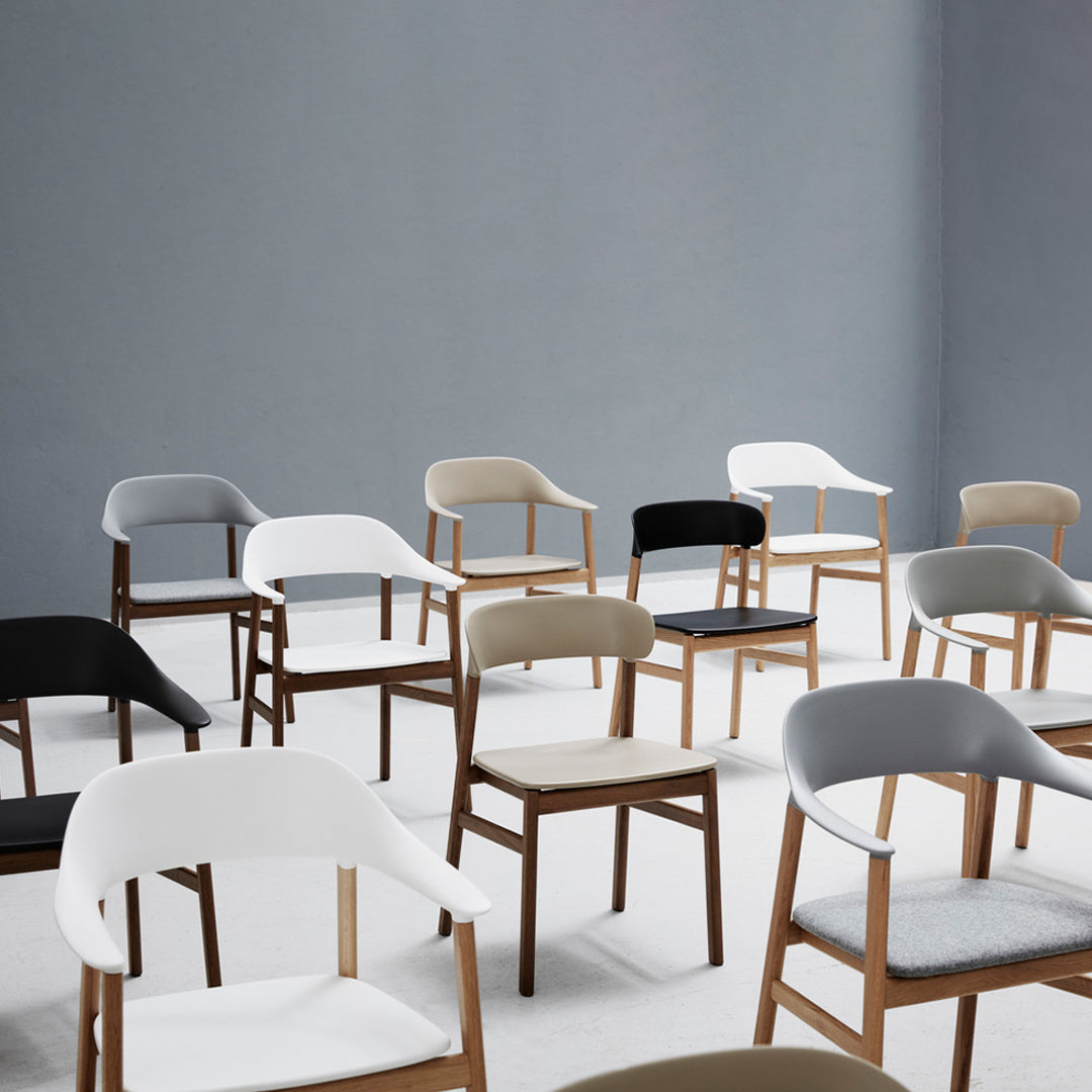Assorted chairs in white, gray, beige, and black with wooden legs against a neutral backdrop. Simple and modern design.