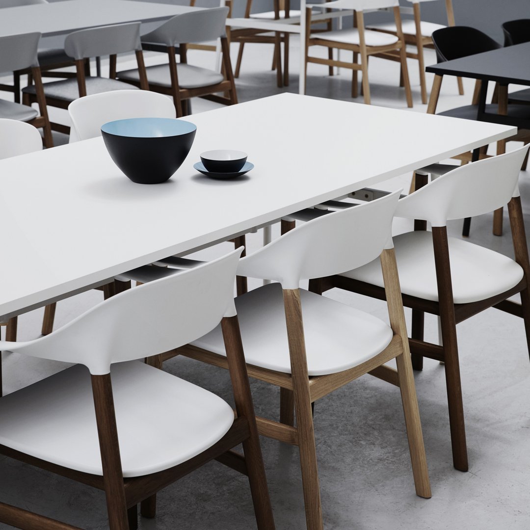 White dining table with modern black and blue bowls; contrasting wooden chairs with white cushions create a stylish vibe.