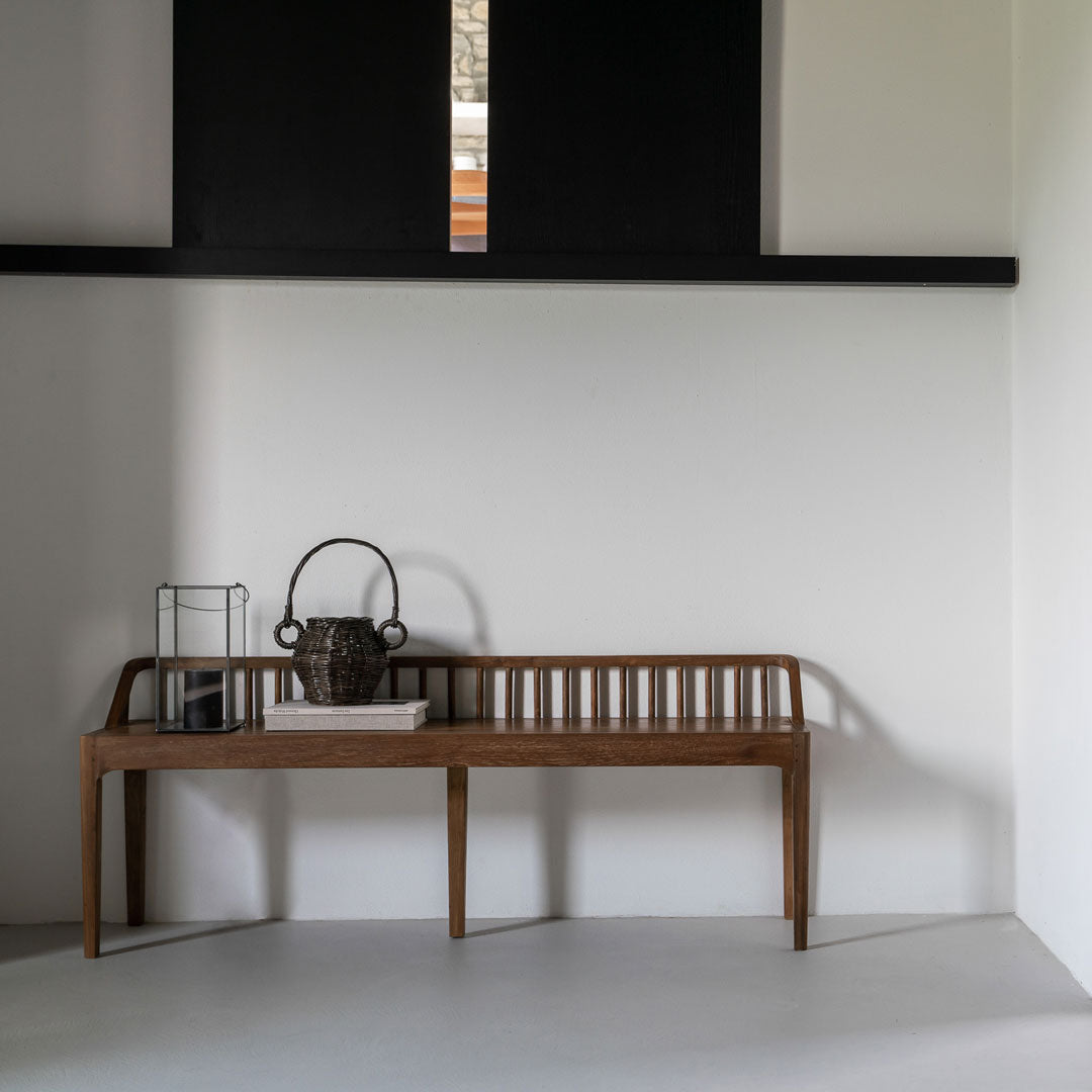 "Natural wooden bench with a slatted back, paired with black and white decor elements against a light wall."