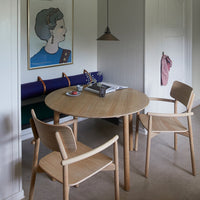"Round wooden table with light oak finish, paired with beige chairs and a blue-accented wall art in a muted color scheme."