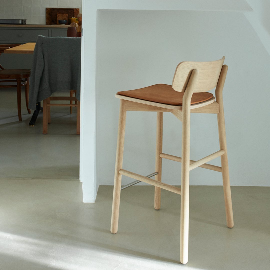 Light wood stool with a warm brown seat, featuring a minimalistic design and smooth, clean lines. Ideal for modern decor.