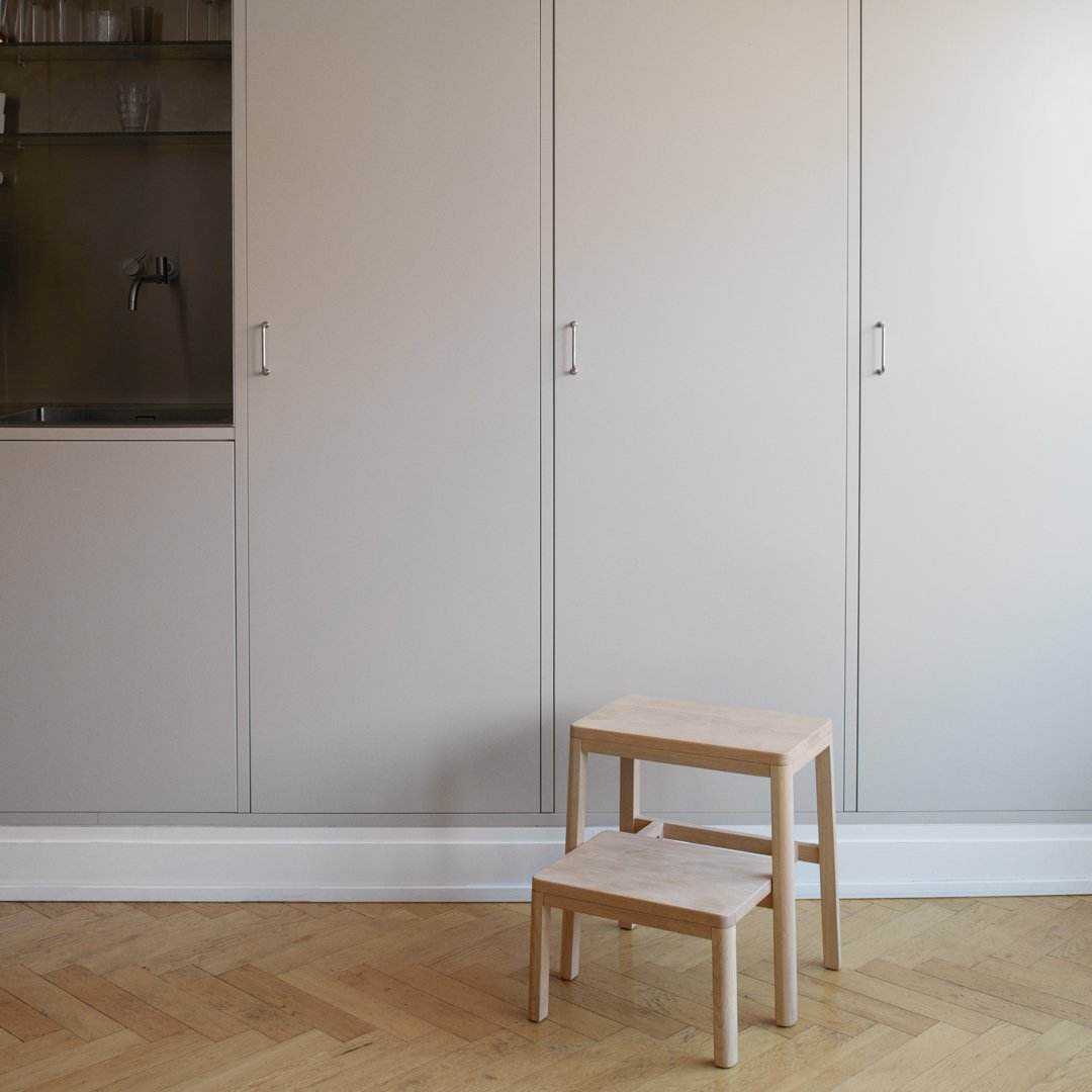 Light wood stacking stools with a minimalistic design against a soft gray backdrop and light wooden flooring.