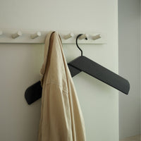 Black hanger holding a beige shirt against a minimalist white wall with white hooks. Clean, modern design.