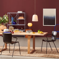 Modern dining room with a wood table, black chairs, burgundy walls, and soft lighting, featuring vibrant fruit accents.