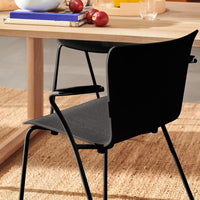 Black chair with a sleek matte finish, sitting on a woven jute rug, against a light wood table.