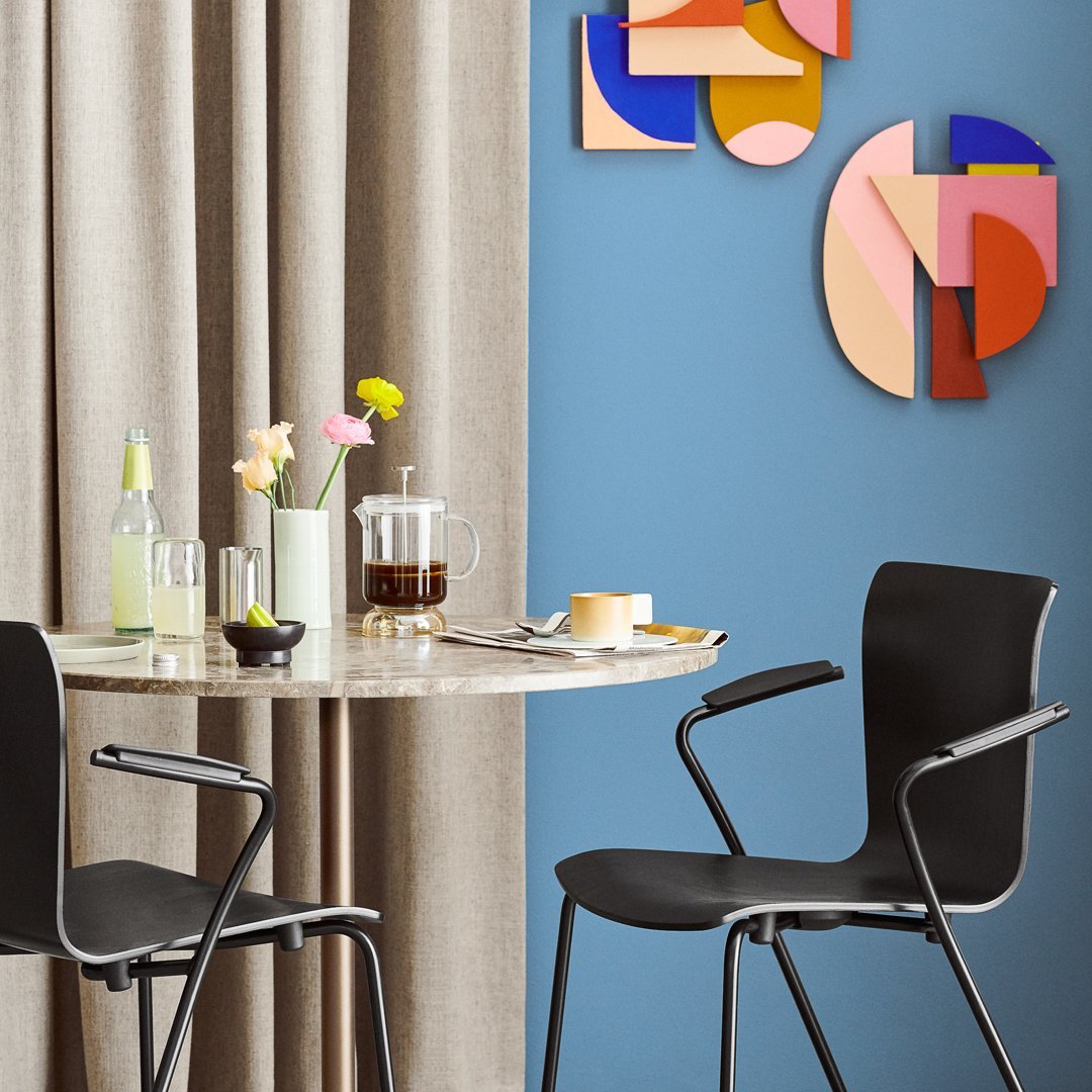 Stylish black chairs around a marble table, with vibrant geometric wall art and soft beige curtains.