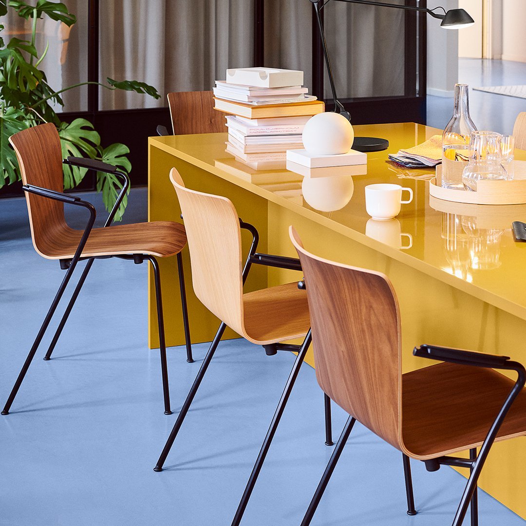 Stylish wooden chairs with curved backs set against a vibrant yellow table and soft blue floor, complemented by greenery.