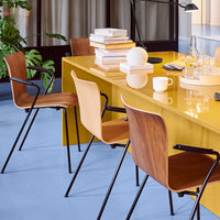 Stylish wooden chairs with curved backs set against a vibrant yellow table and soft blue floor, complemented by greenery.