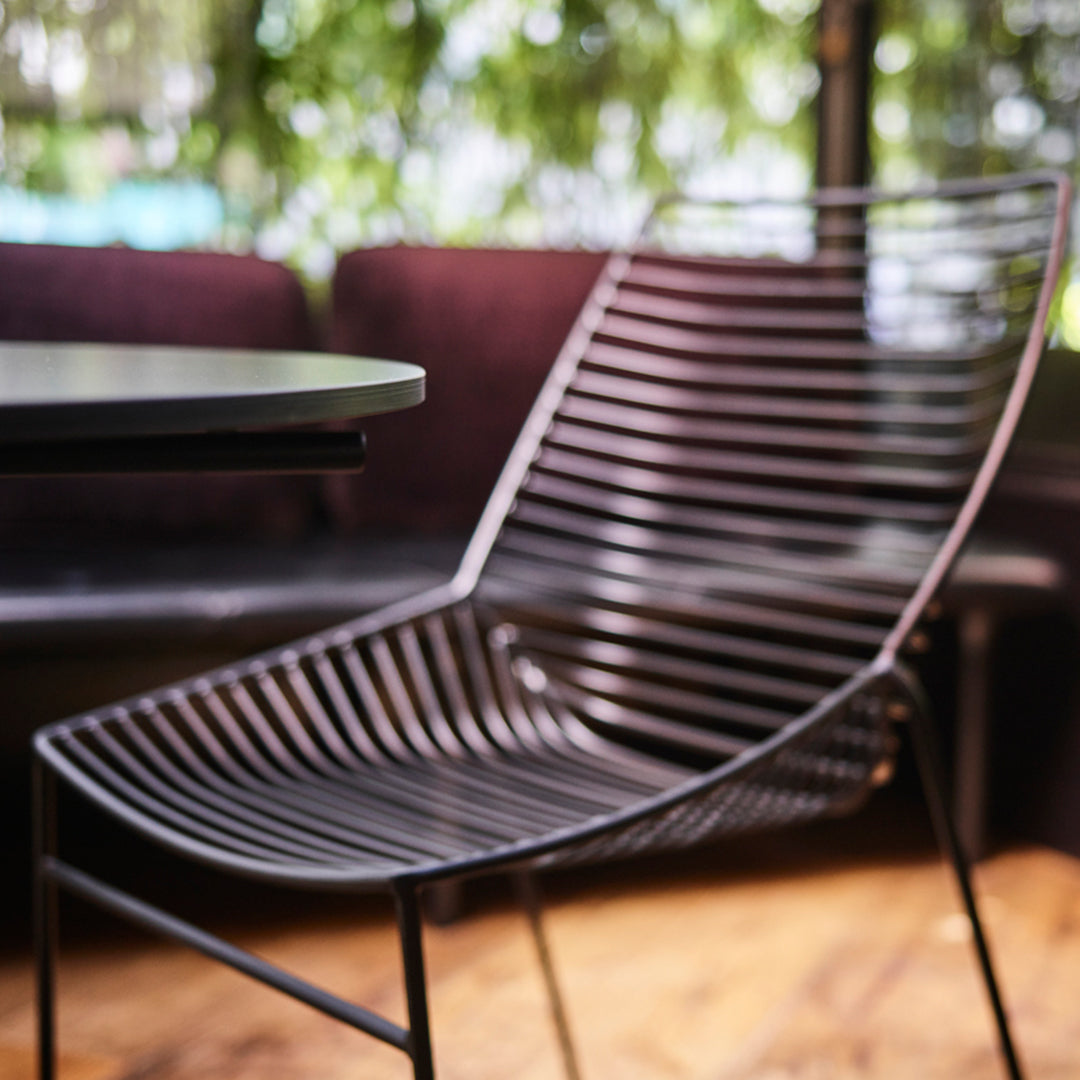 Black striped metal chair with a sleek design against a blurred backdrop of purple and green hues.