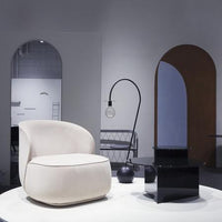 Cream-colored accent chair beside a sleek black table, set against minimalist gray and warm wooden tones.