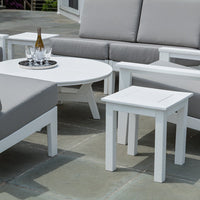 Modern outdoor furniture set featuring white tables and gray cushions on a stone patio. Minimalist design with clean lines.