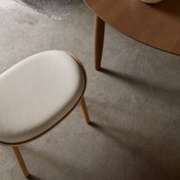 Light beige cushion with natural wood legs paired with a round wooden table on a textured gray floor.
