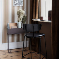 Black metal chair against a striped beige wall, featuring earthy tones and smooth textures. Elegant minimalistic design.