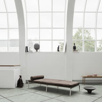 "Elegant brown chaise lounge on a light turquoise patterned floor, set against bright white walls and large windows."