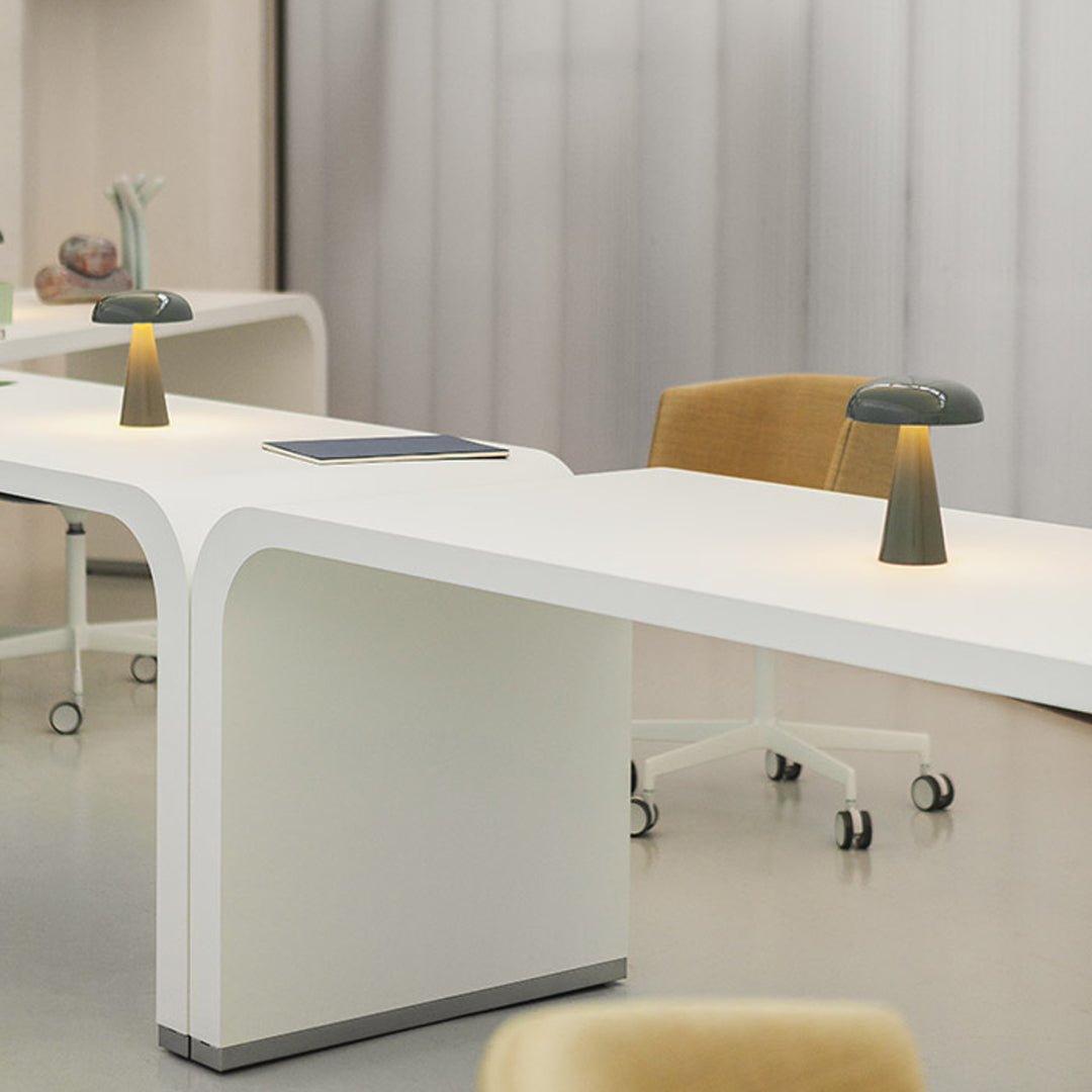 Sleek white desk with smooth curves, complemented by soft yellow chair and muted gray-green lamp. Modern and minimalist design.