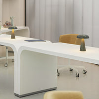 Sleek white desk with smooth curves, complemented by soft yellow chair and muted gray-green lamp. Modern and minimalist design.
