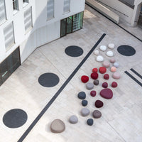 Colorful circular cushions in shades of red, pink, gray, and black arranged on a light stone floor.