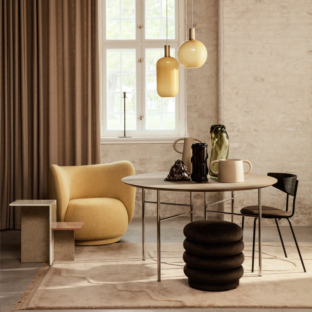 Modern living space featuring beige curtains, yellow accent chair, black stool, and round table in earthy tones.