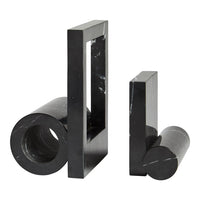 Black geometric decorative objects with sleek polished surfaces and varied shapes, including cylindrical and rectangular forms.