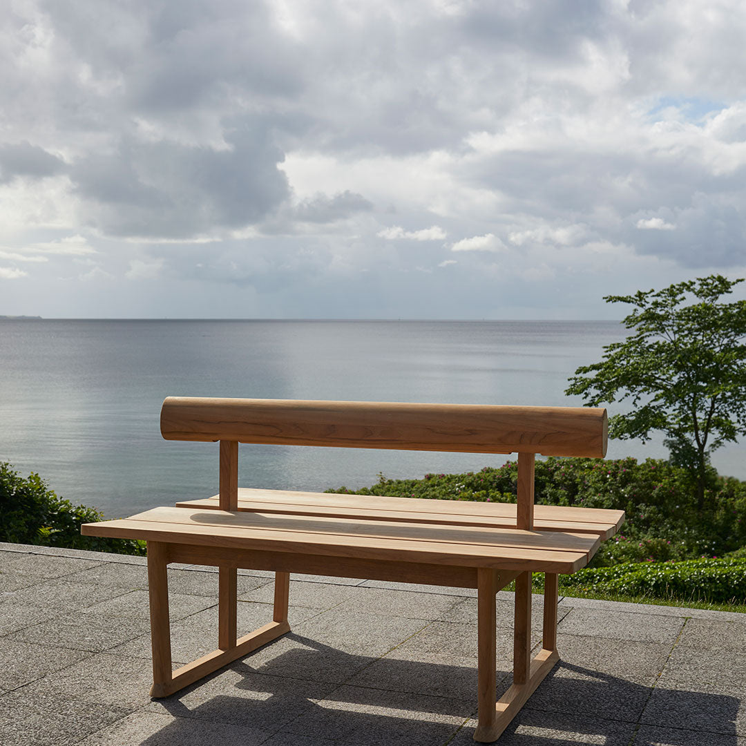 Natural wood bench in light oak finish, smooth surface, minimalist design against a serene outdoor backdrop.