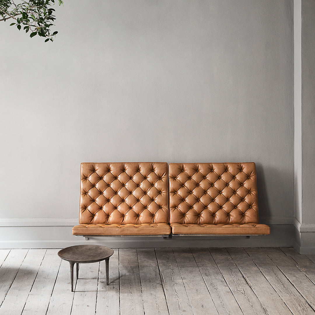 Tan tufted leather sofa with a geometric pattern, set against a minimalist gray wall and wooden floor.