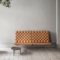 Tan tufted leather sofa with a geometric pattern, set against a minimalist gray wall and wooden floor.