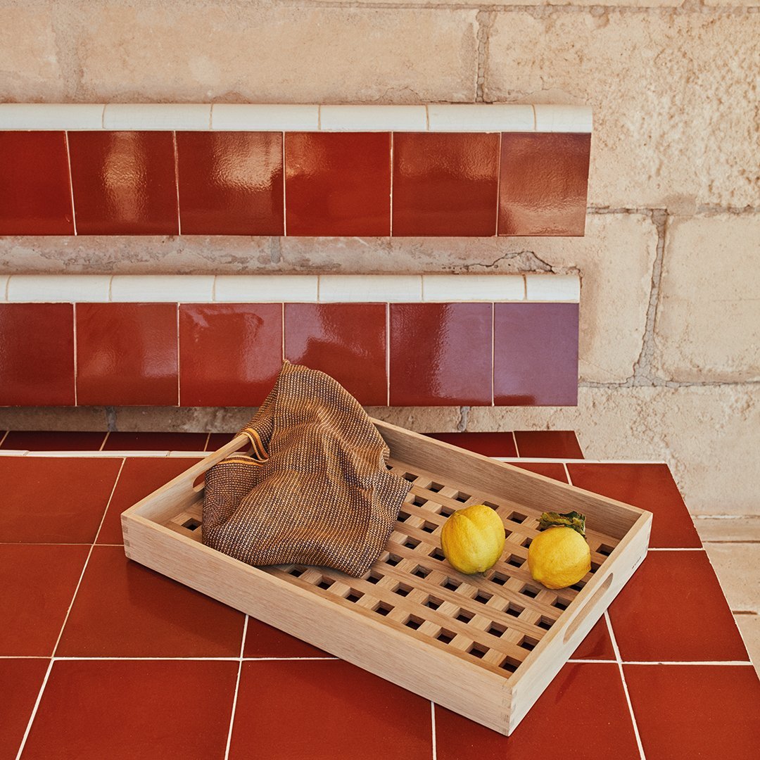 "Red and white patterned tiles with a wooden tray and yellow lemons on a matching red tiled surface."
