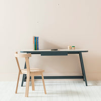 Light wood chair with a blue and beige desk against a soft pink wall, featuring simple, modern design.