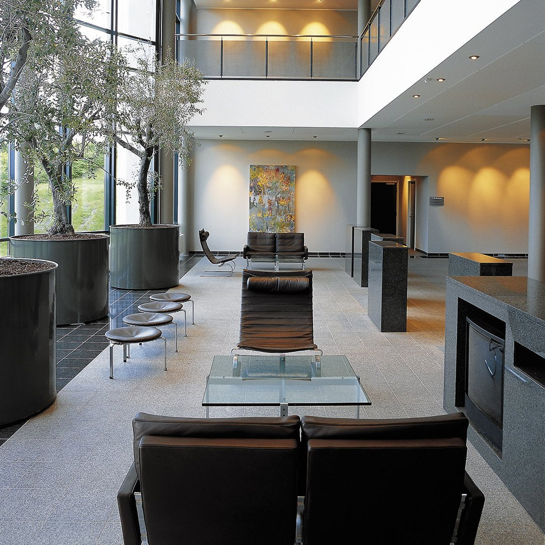 Modern lounge area with sleek black chairs, glass accents, and soft gray tones, surrounded by natural greenery.