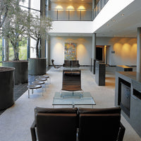 Modern lounge area with sleek black chairs, glass accents, and soft gray tones, surrounded by natural greenery.