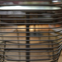 Black metal chair with horizontal slat pattern against a blurred wooden background. Modern and sleek design.