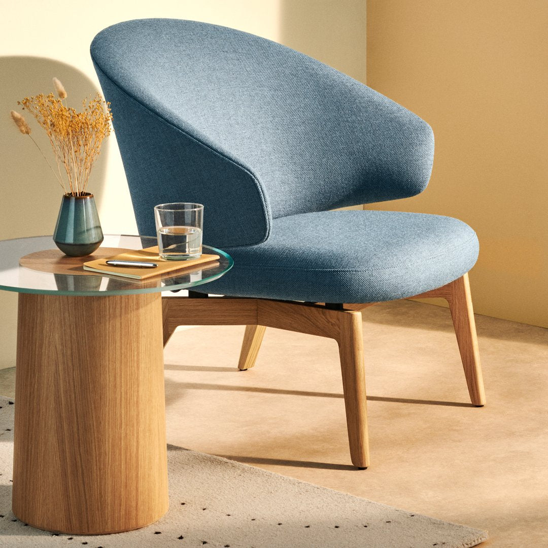 Modern blue upholstered chair with a smooth curved back, paired with a wooden side table and minimalistic decor.