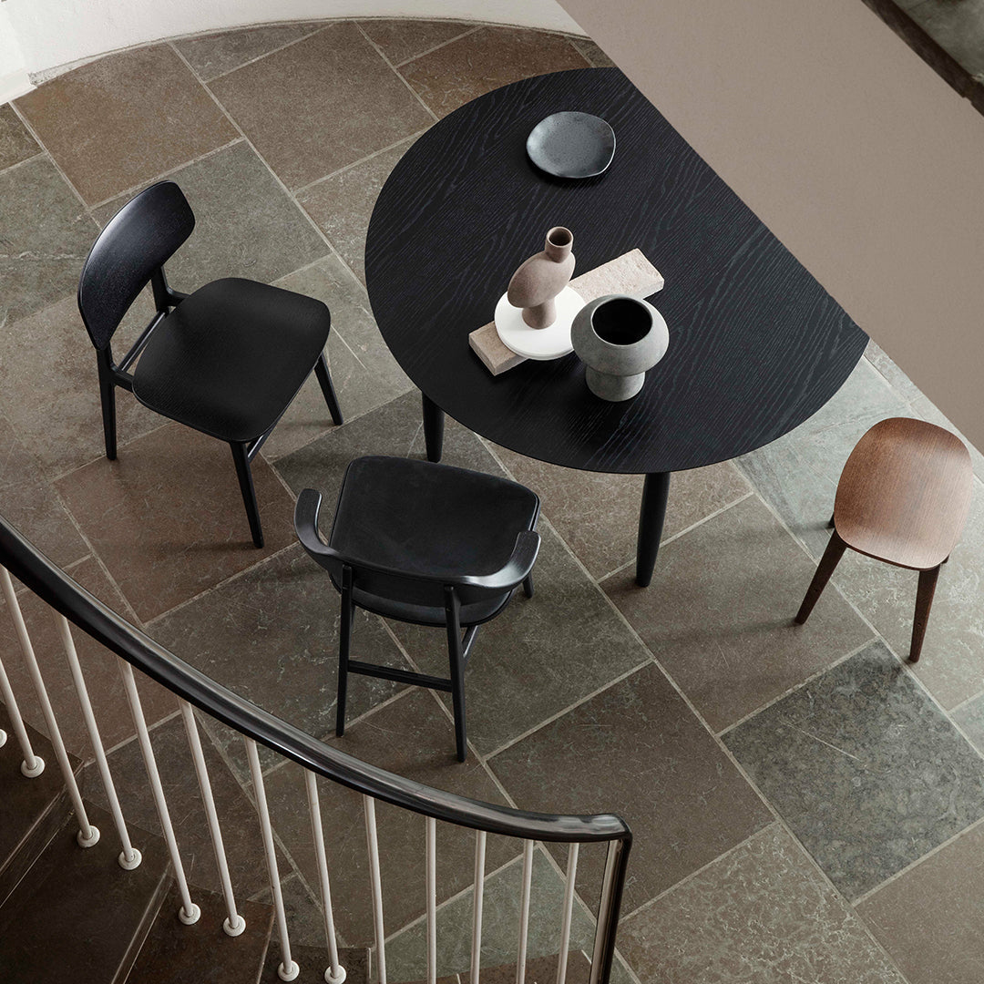 Stylish round black table with cream and muted gray accents, surrounded by black, tan, and pink chairs on a textured stone floor.